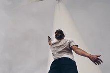 Eine Person steht unterhalb eines Windrads und reckt einen Arm in die Höhe